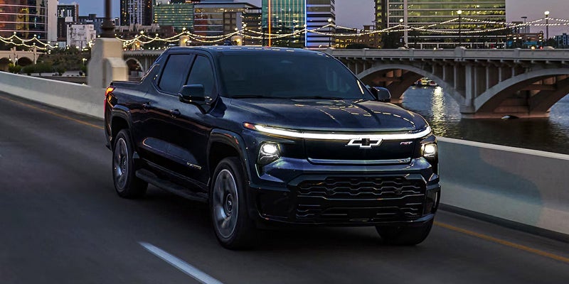 Black 2025 Chevrolet Silverado EV driving over bridge with headlights on